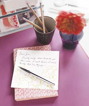 Pen and half-written letter next to a cup of pencils and a flower